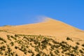 Dune against the background of a bright blue sky. The wind blows the sand off the ridge of the dune